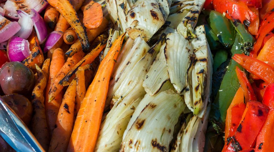 A mix of colorful grilled vegetables with metal serving tongs