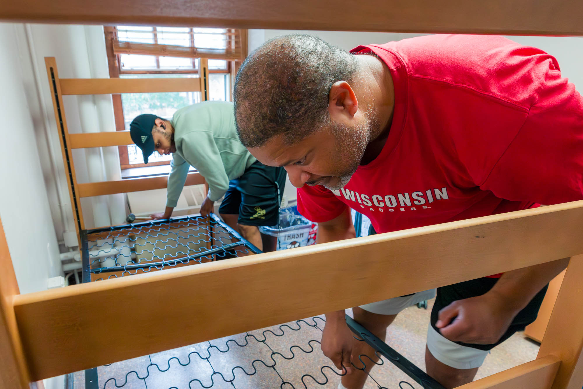 Two people working on lofting a bed in a residence hall room