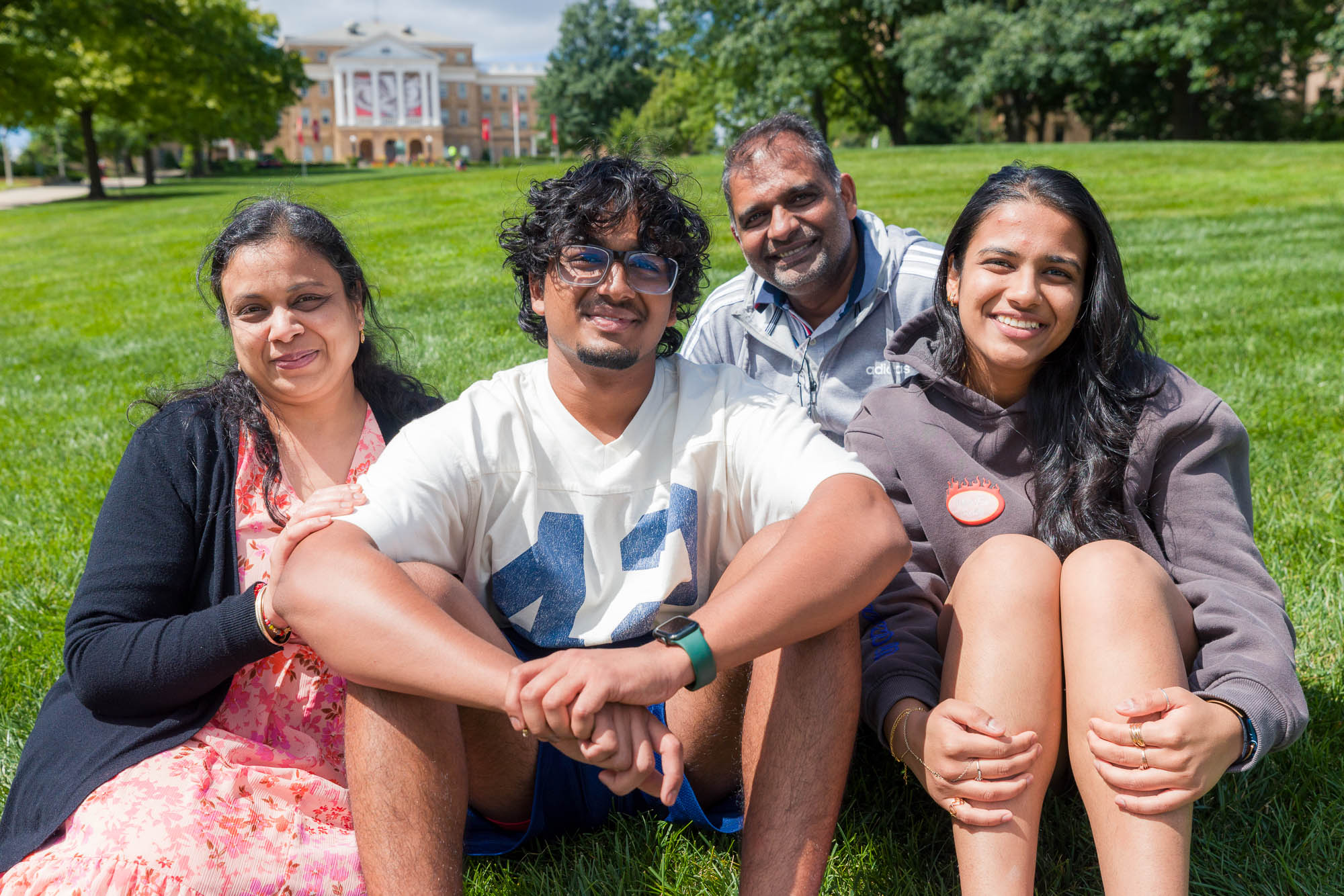 Four people pose for a photo while sitting on grass