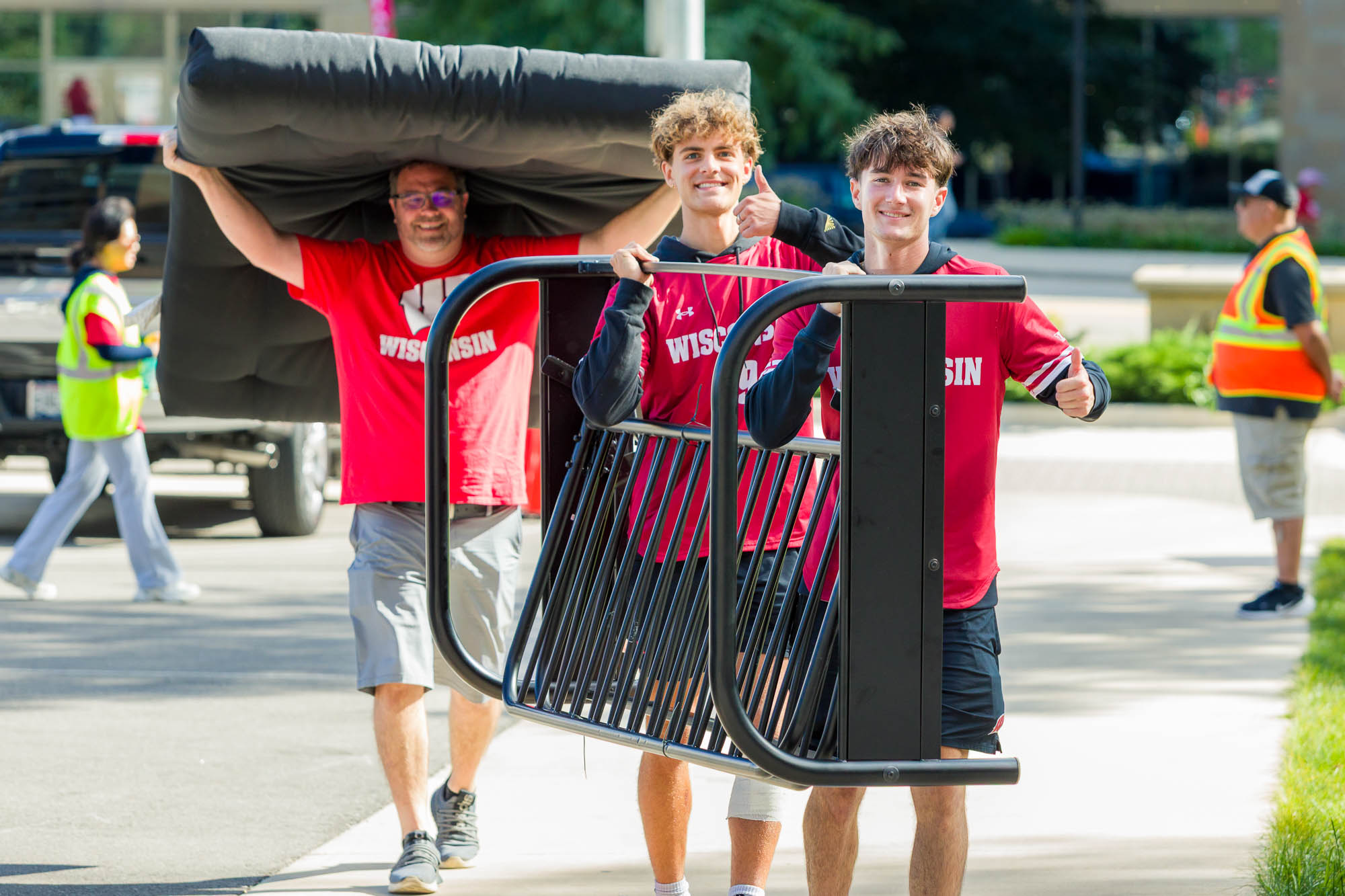 Two people moving a futon while a third person moves a mattress in the background