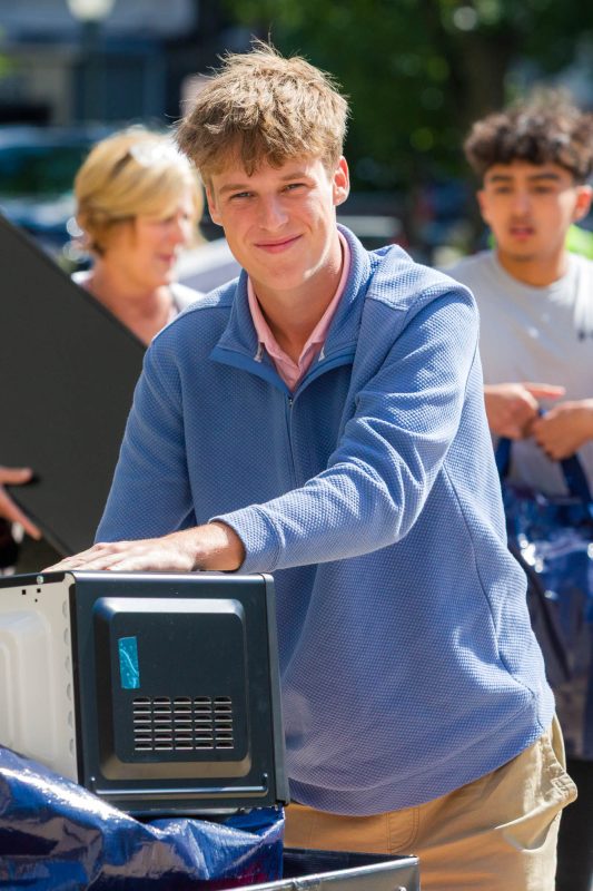 A person holds a microwave on a storage cart while smiling