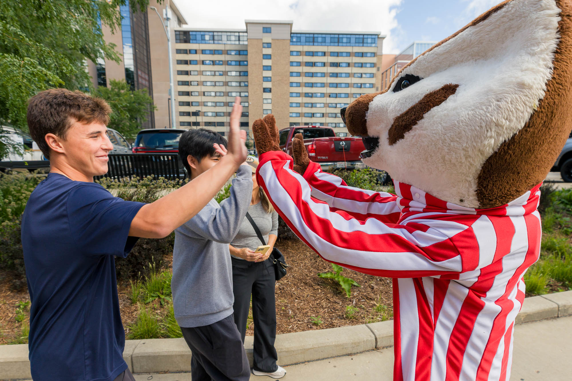 Two people give high fives to Bucky Badger