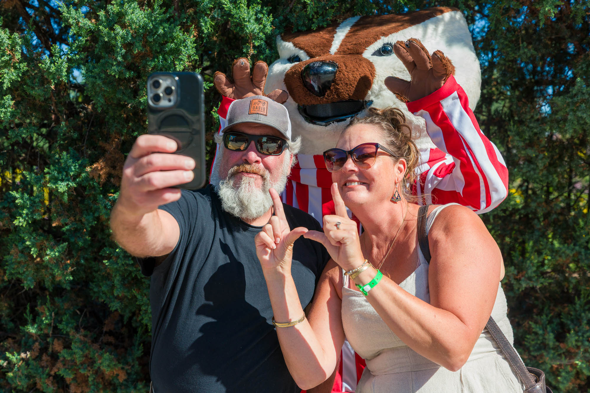 Two people taking a selfie with a phone with Bucky Badger in the background