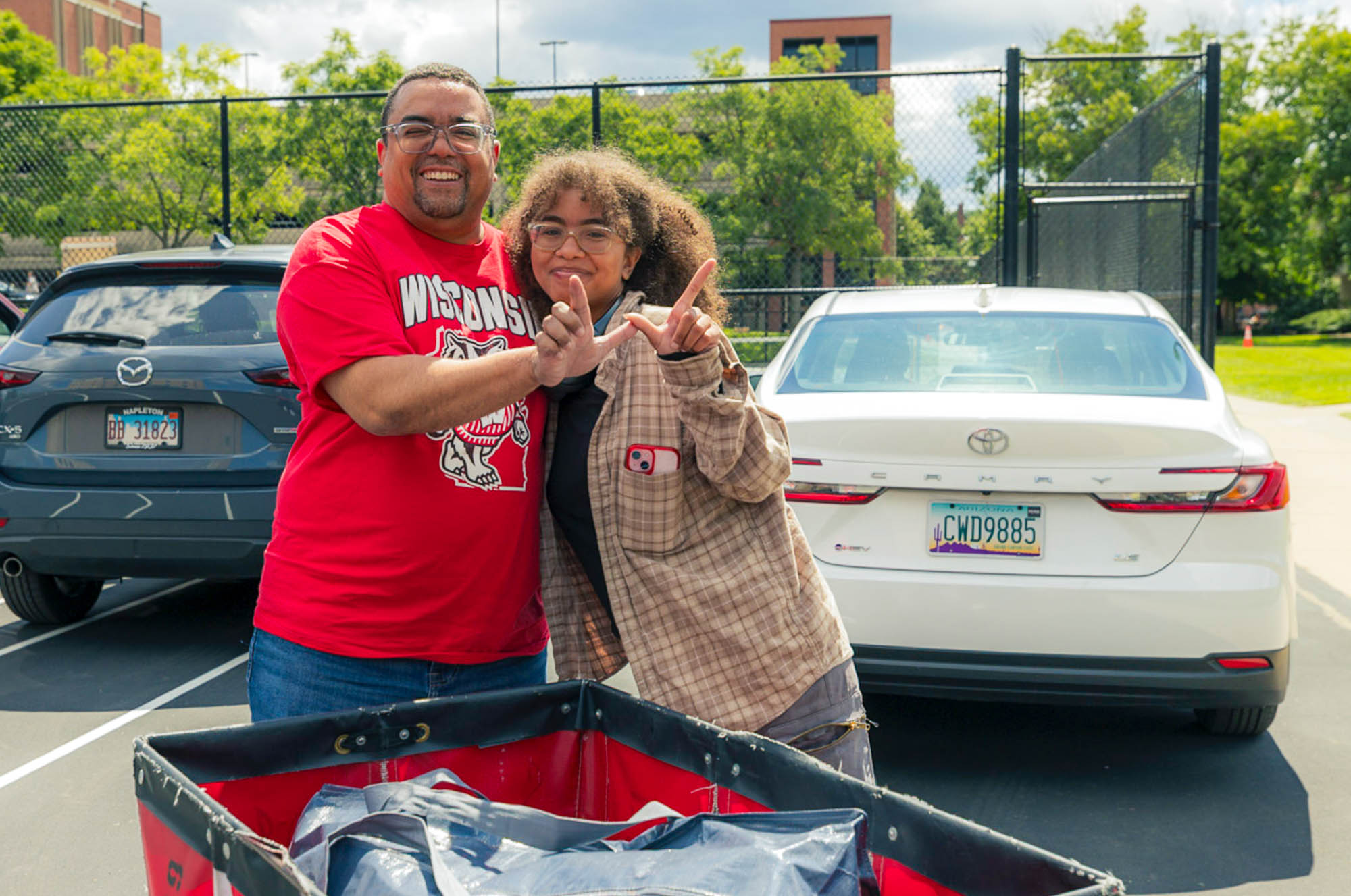 Two people form a "W" with their hands behind a moving cart with their car in the background