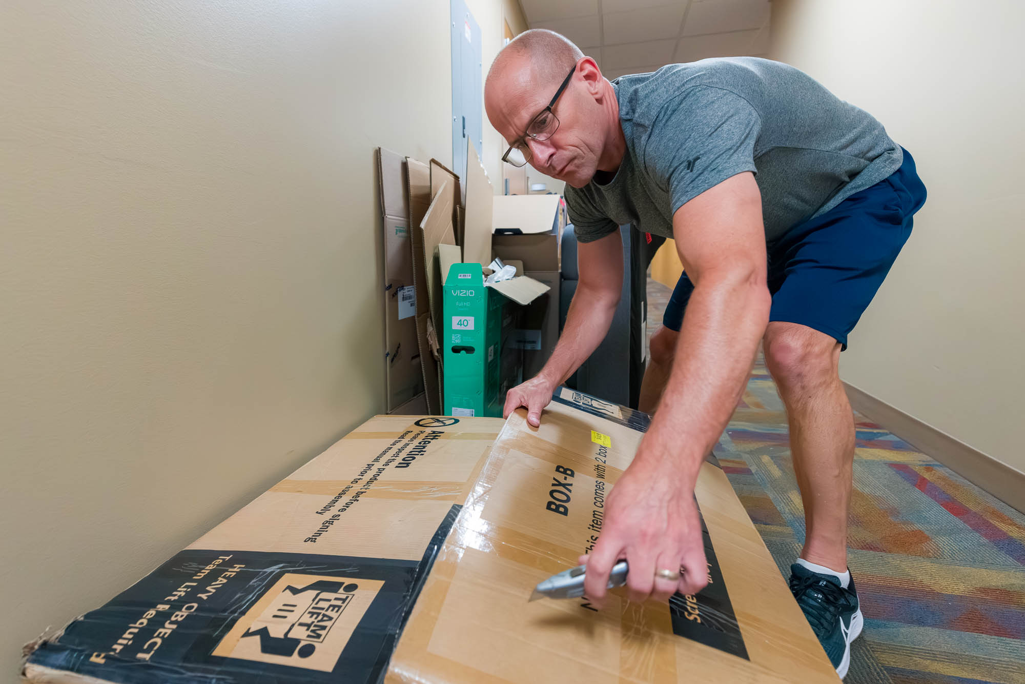 One person uses a retractable knife to cut open a box in a hallway