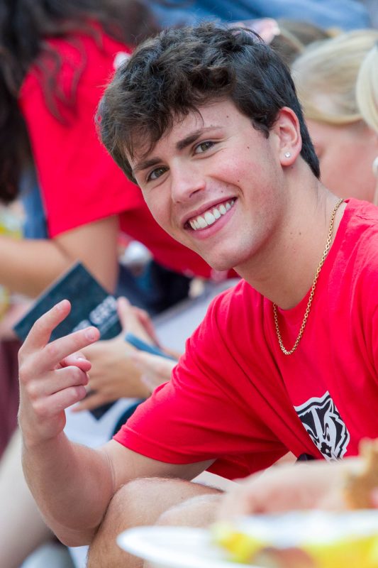 A person smiles at the camera while holding up two fingers in a peace sign gesture