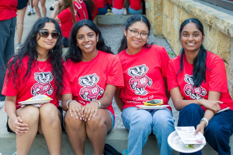 Four people smile for a photo while sitting on a concrete barrier