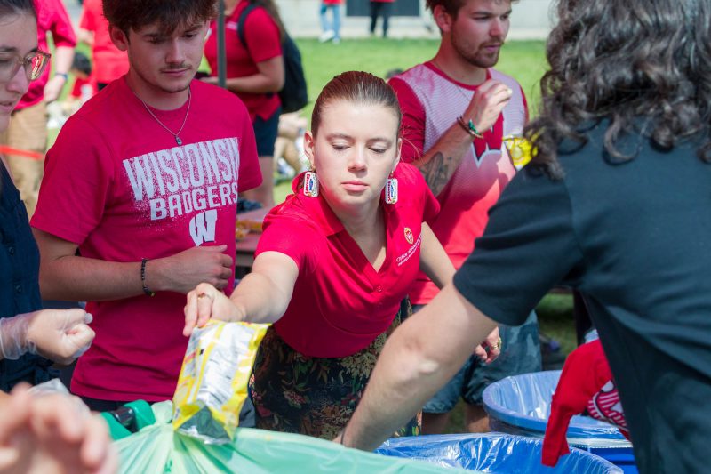 A person in the middle of a group of other people throws a bag into a trash bin