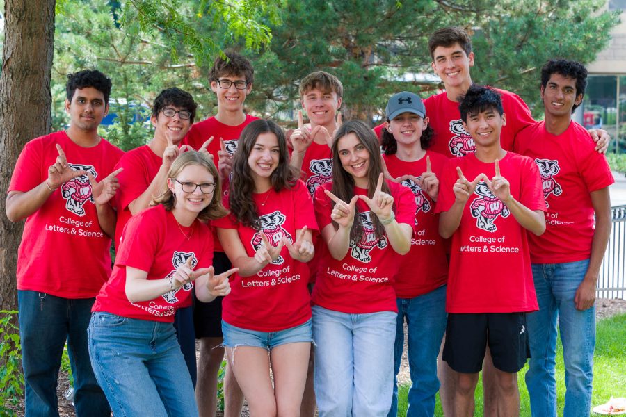 A group of people pose for a photo near trees while forming the letter "W" with their hands
