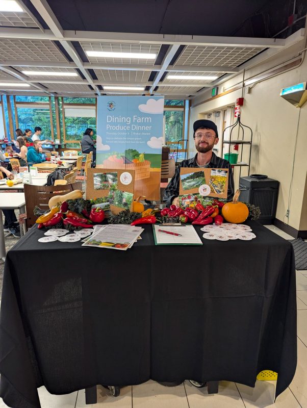Staff member posing at the Dining Farm Produce Dinner info table at Rheta's Market
