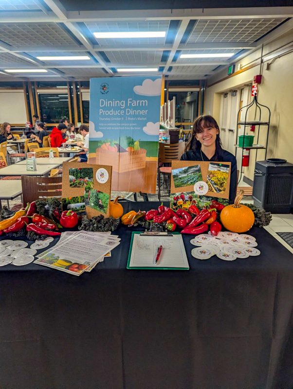 Student staff member posing at the Dining Farm Produce Dinner info table at Rheta's Market