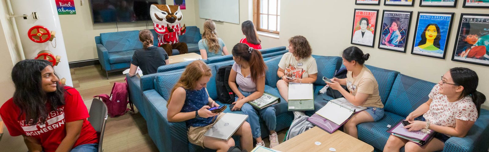 A group of people sit in a lounge studying while Bucky Badger makes an appearance