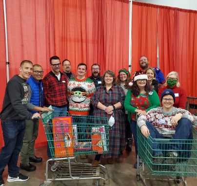 Staff posing for a group photo in holiday apparel with shopping carts filled with items