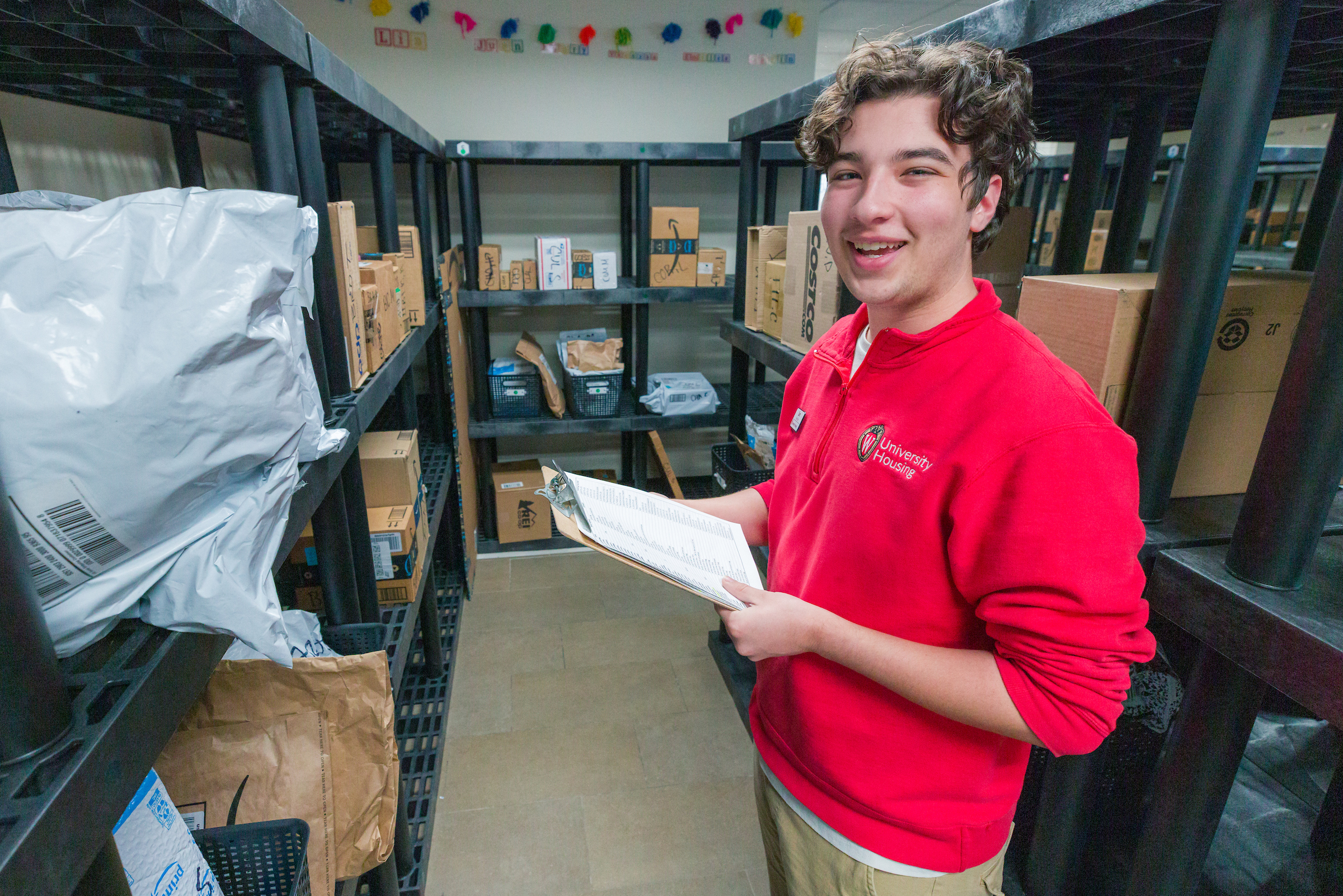 A Housing student staff member smiles for a photo among packages on shelves