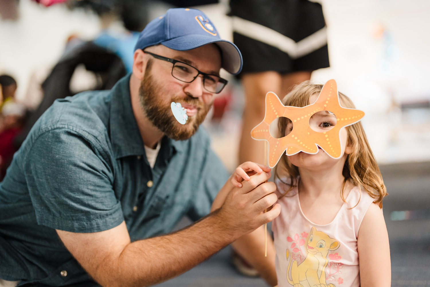 An adult holds a crafted mask in front of a child's face for a photo