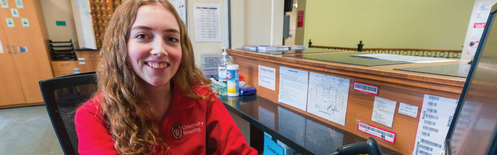 A Housing staff member smiling for a photo while sitting at a hall desk
