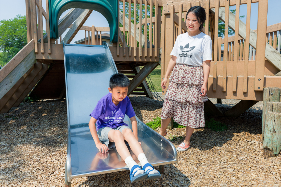 Child going down slide while mother watches at an outdoor play area in Eagle Heights