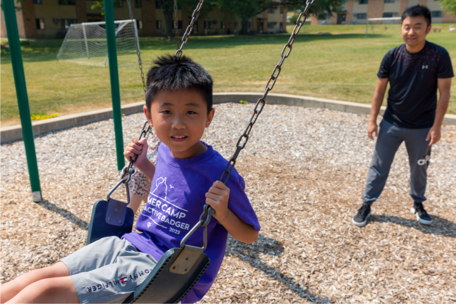 Child swinging and smiling on and outdoor play area at University Apartments