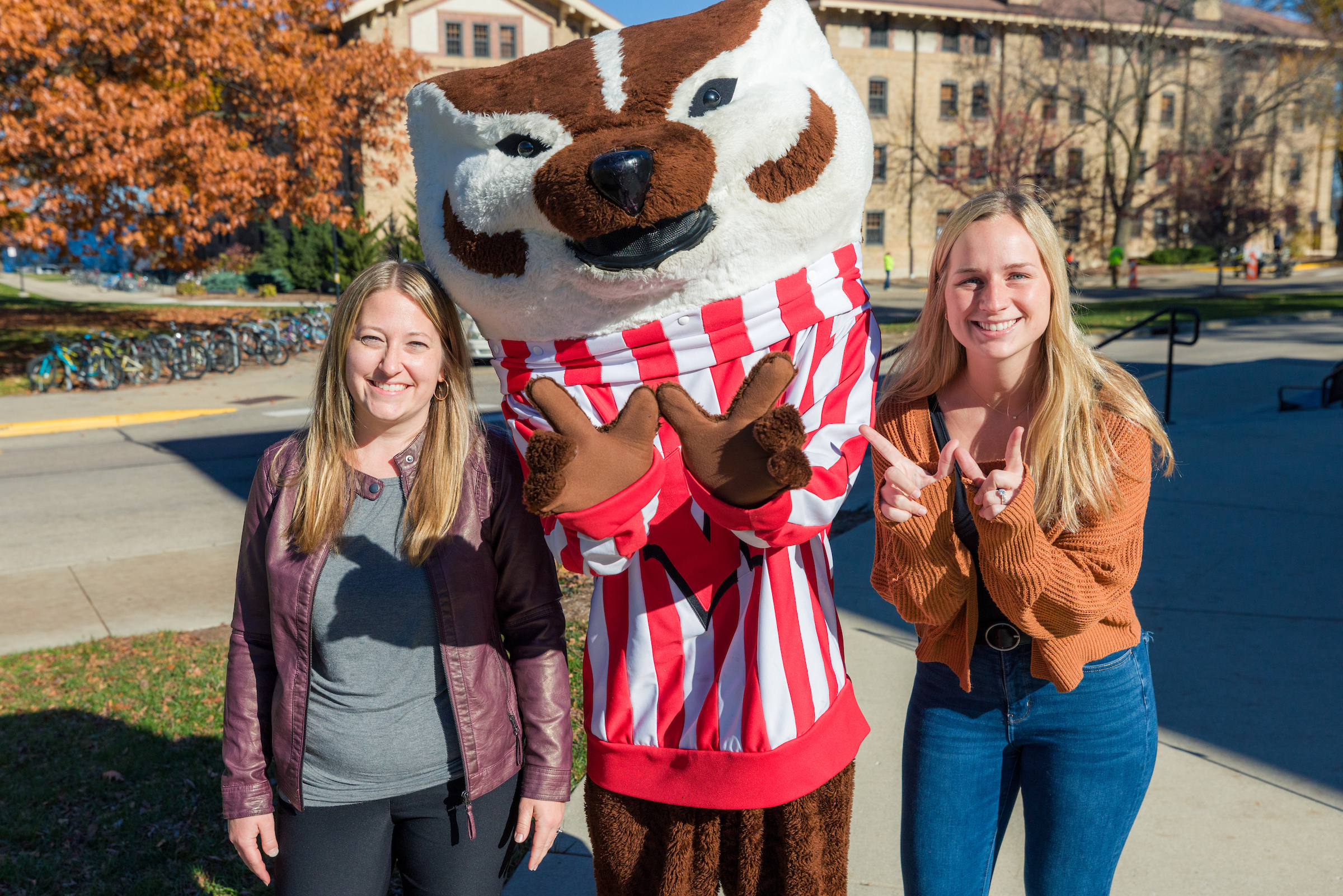 Two staff members pose for a photo with Bucky Badger