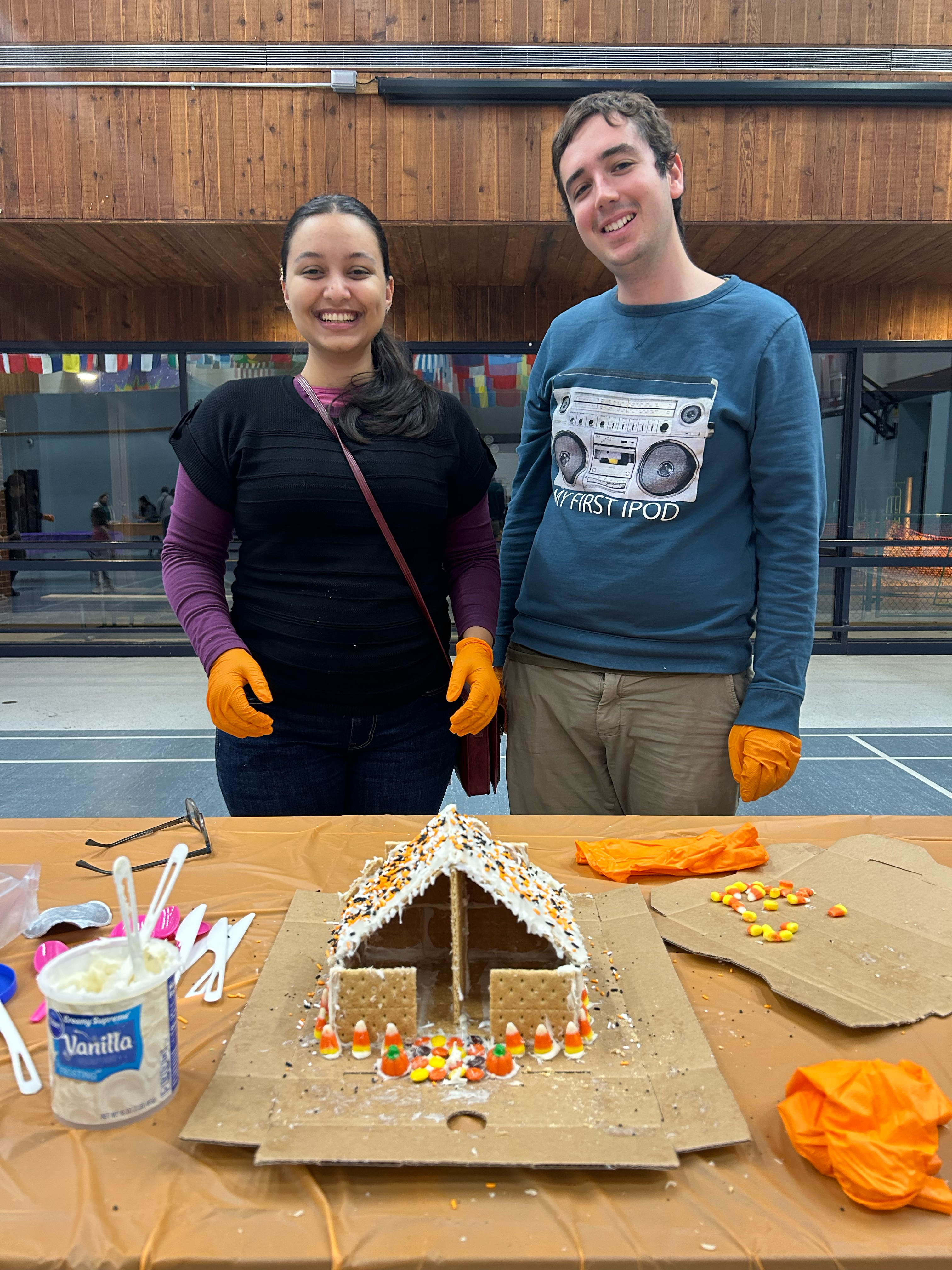 Man and Women smiling in background with gingerbread haunted house