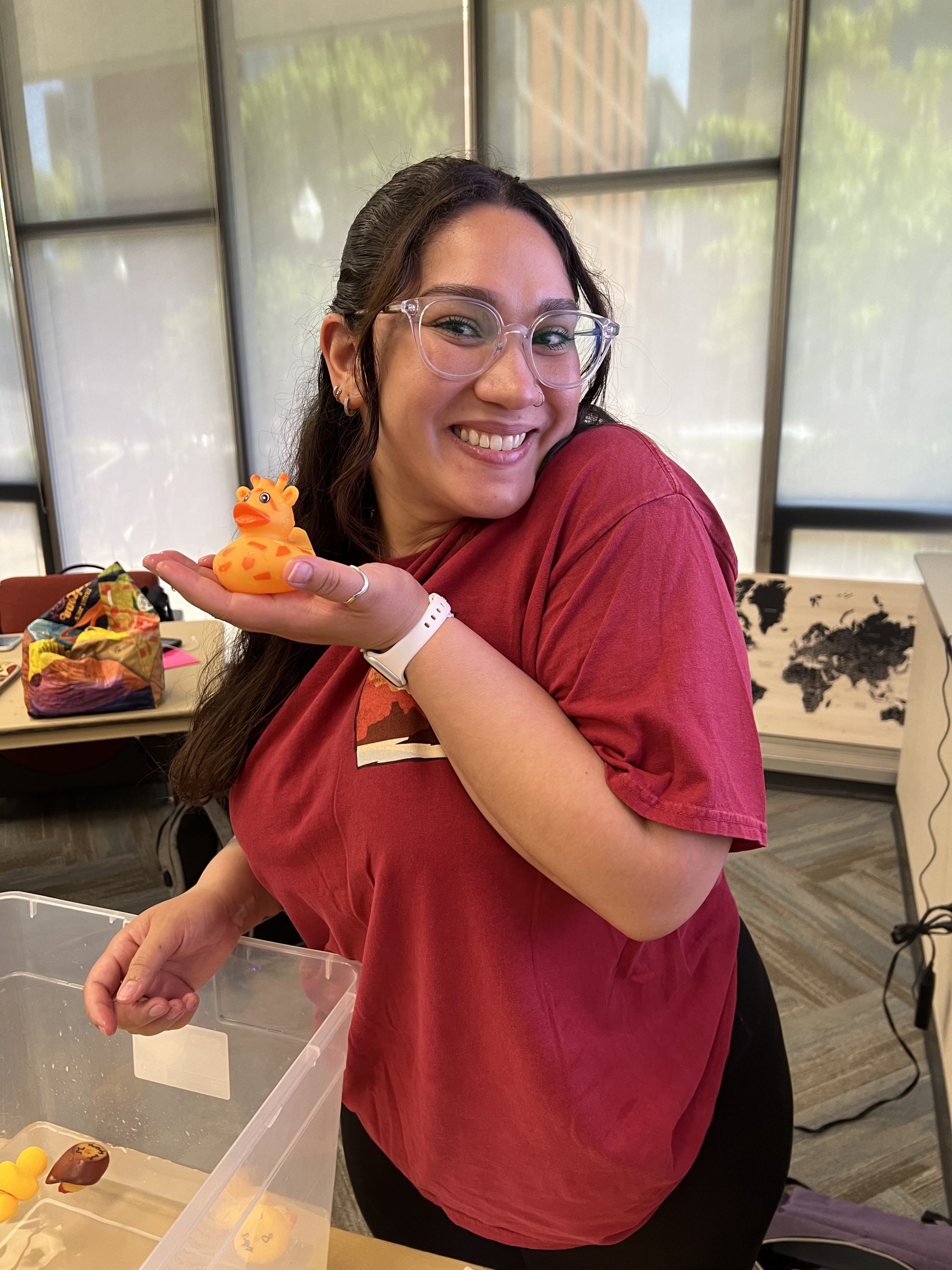 A brown haired women with glasses smiling and holding a rubber ducky