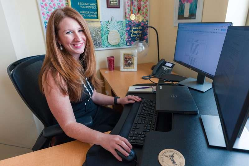 women with red hair smiling at the camera while working on her computer