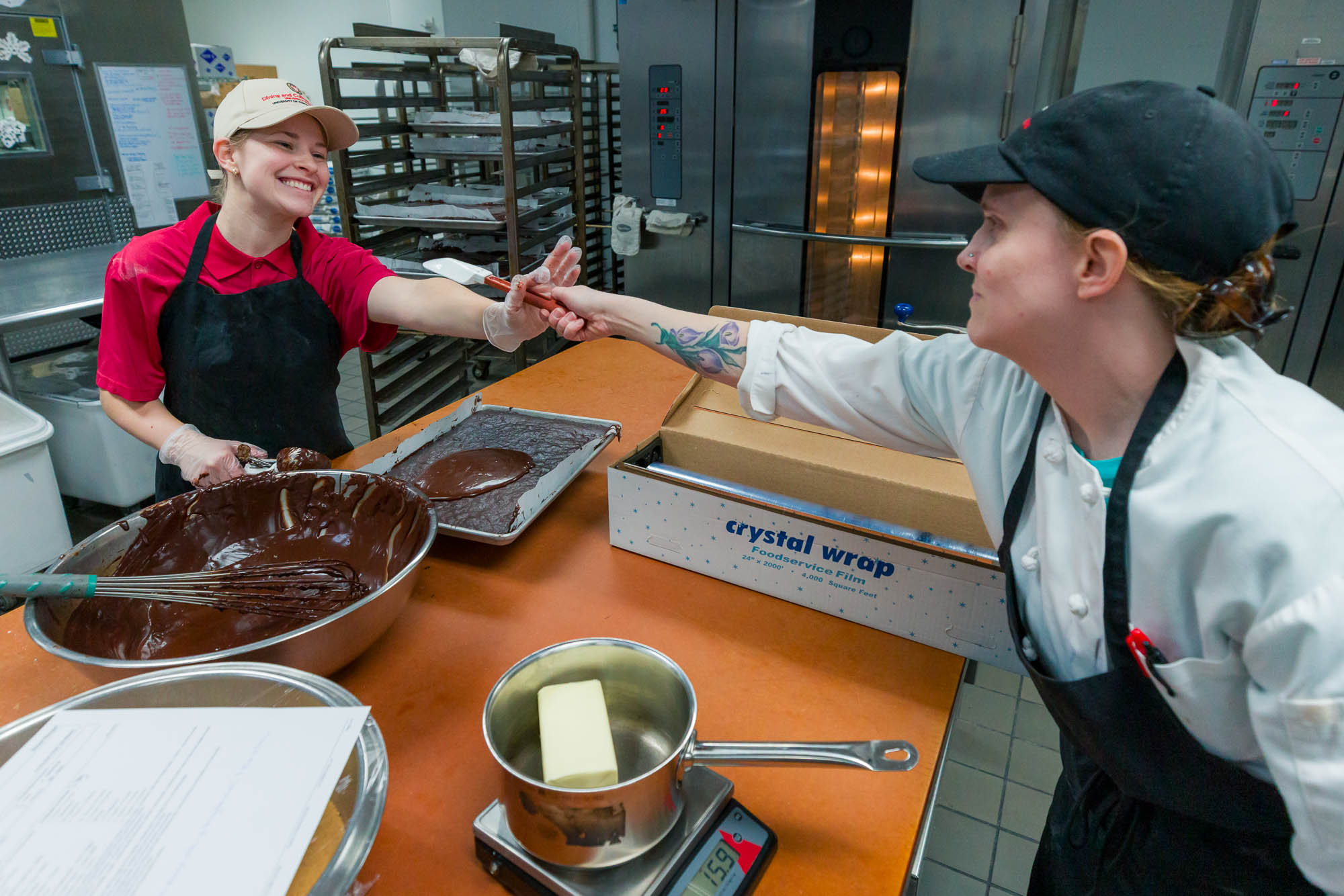 Emma Zeller takes a spatula from a baker in the kitchen at Gordon Dining & Event Center.