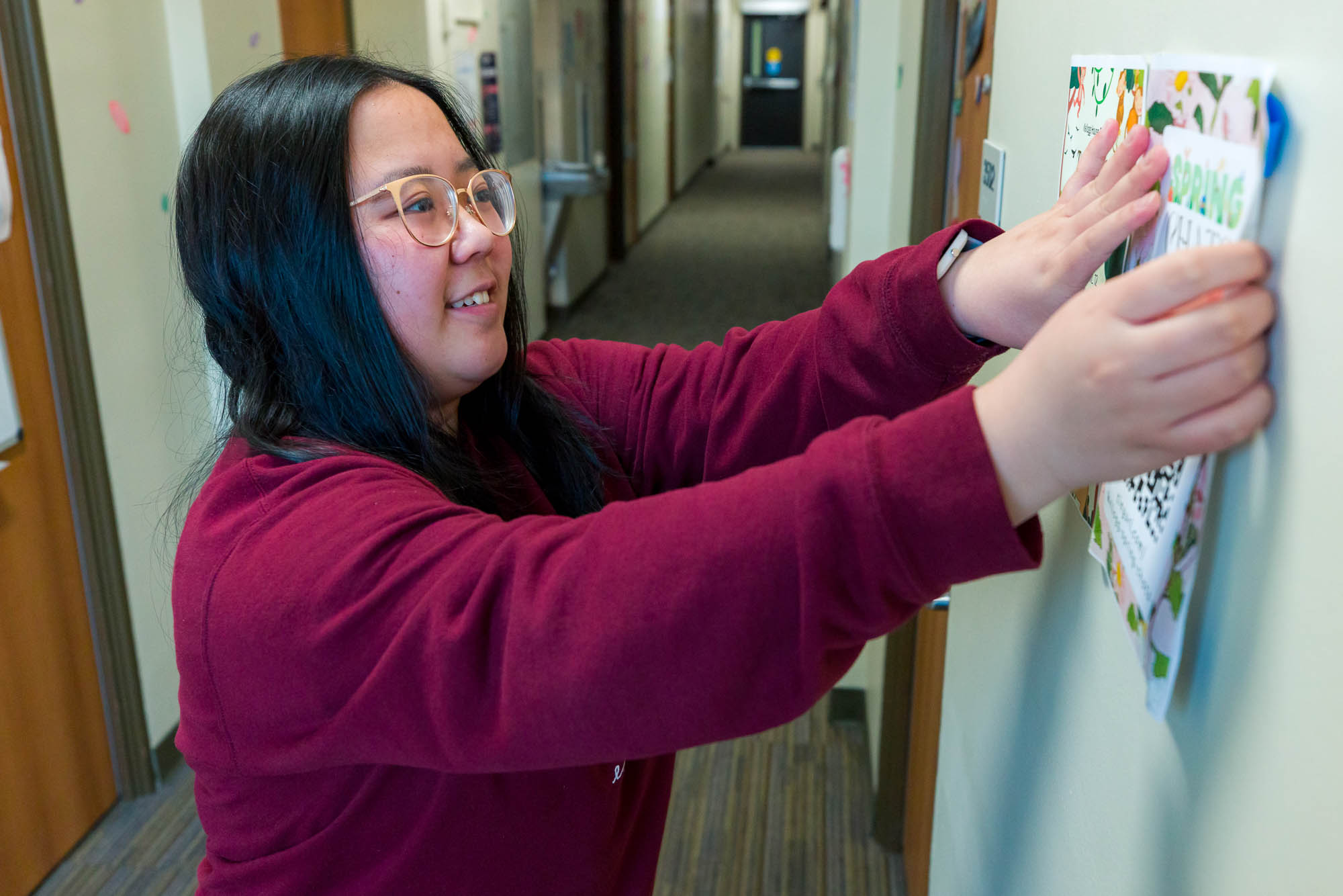 Carol Sze puts up promotional posters in the hallway of Waters Residence Hall.