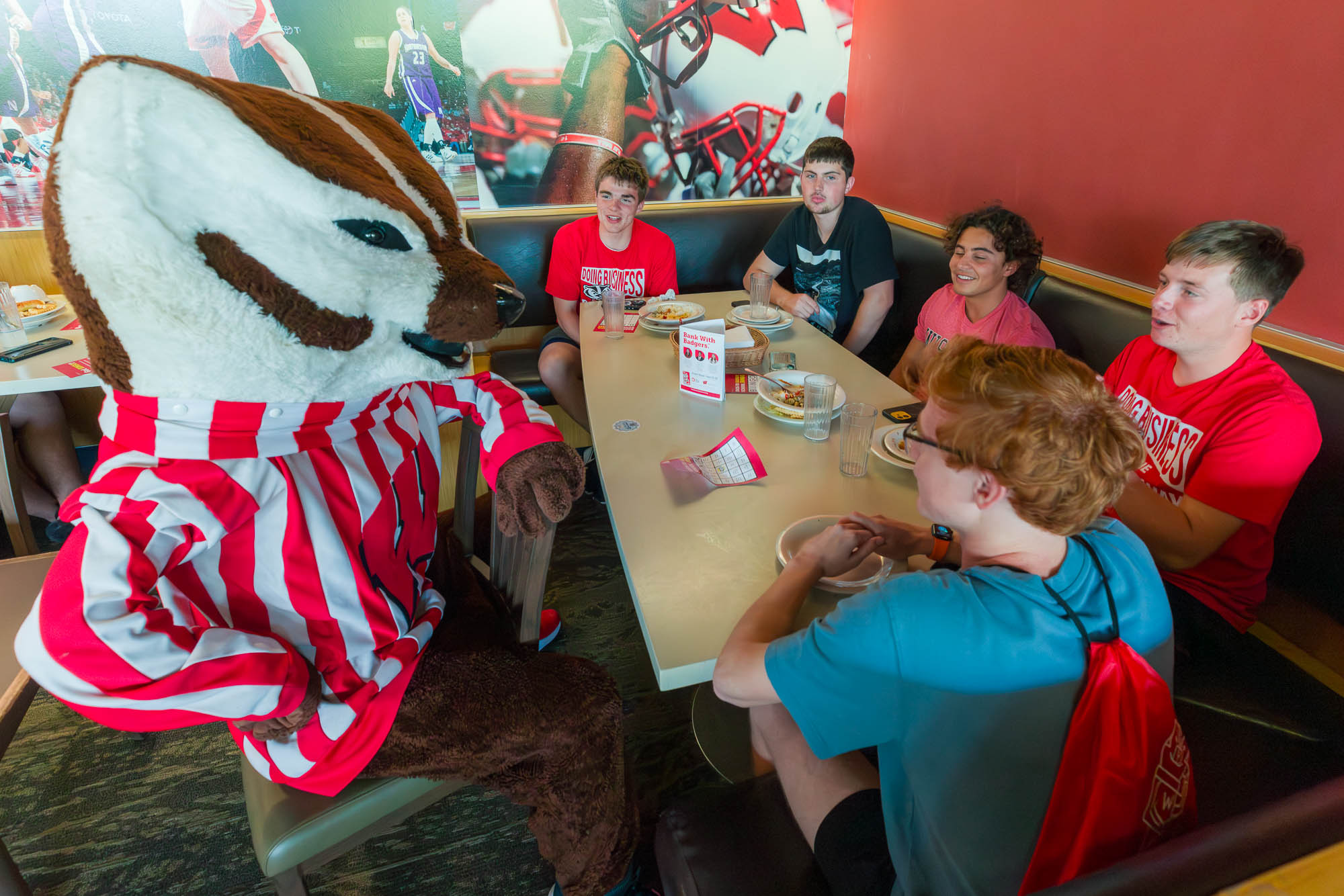 Five people sit at a table eating with Bucky Badger