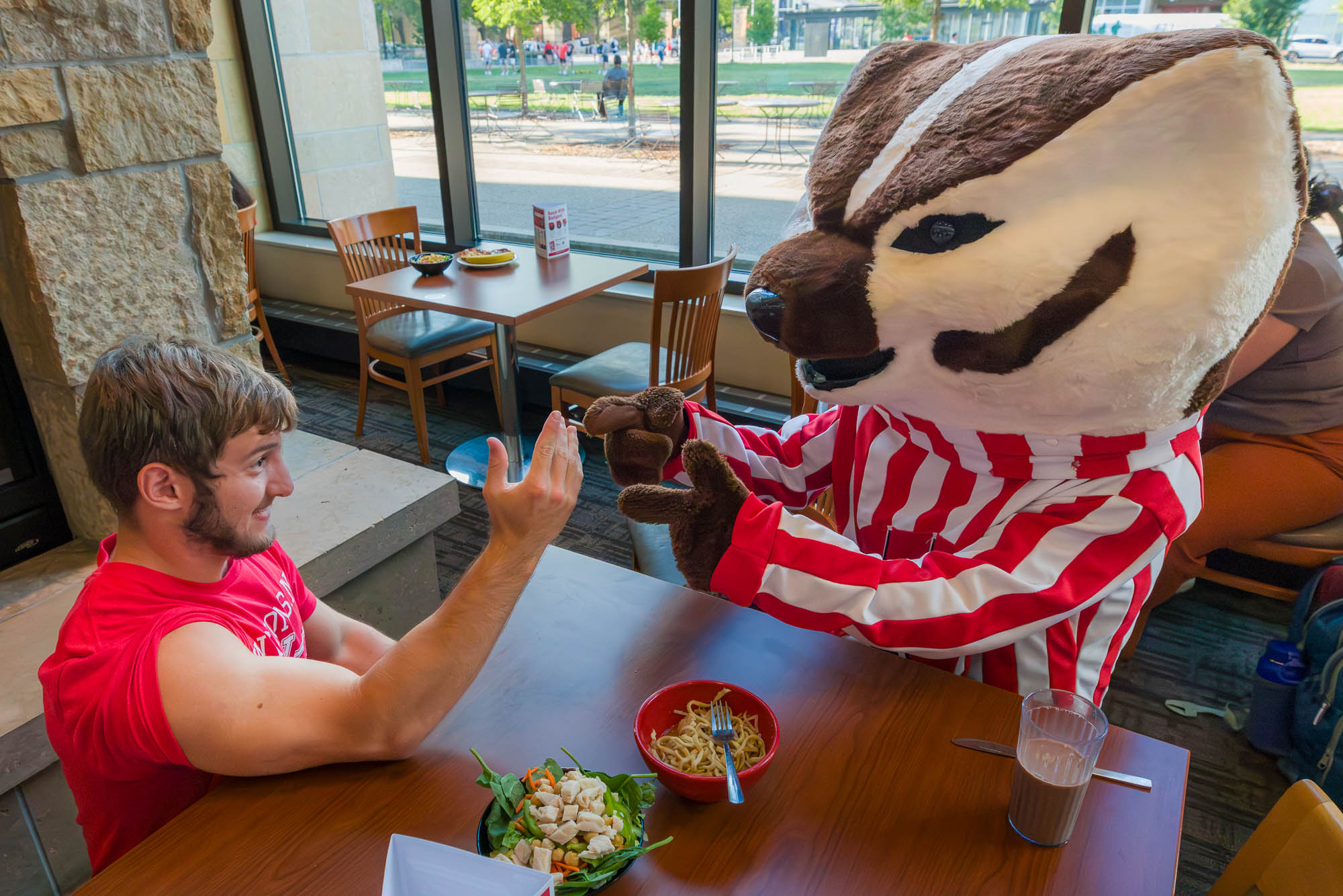 Bucky Badger and one person get ready to arm wrestle at a table
