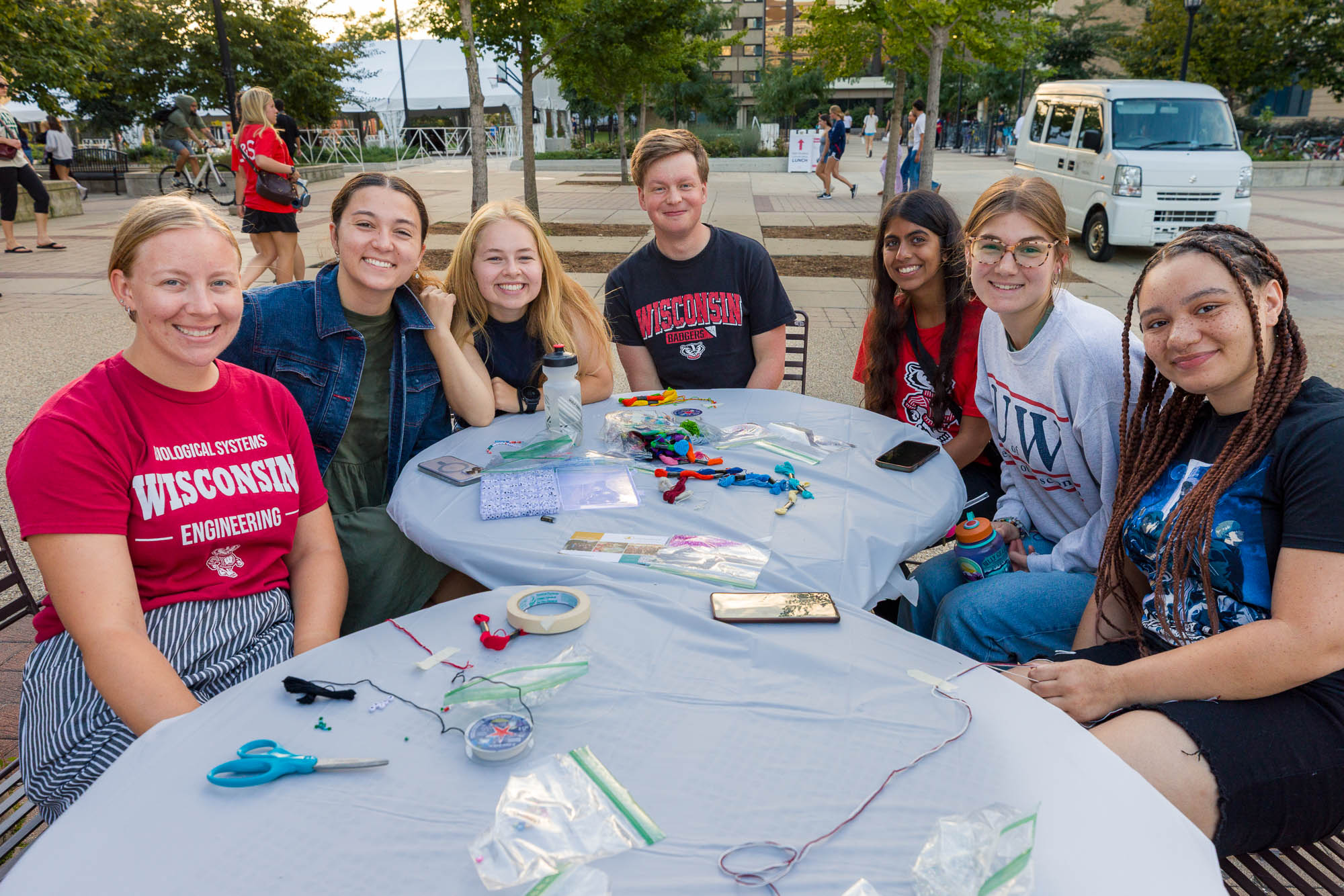 Seven people pose for a photo at tables outside while making bracelets