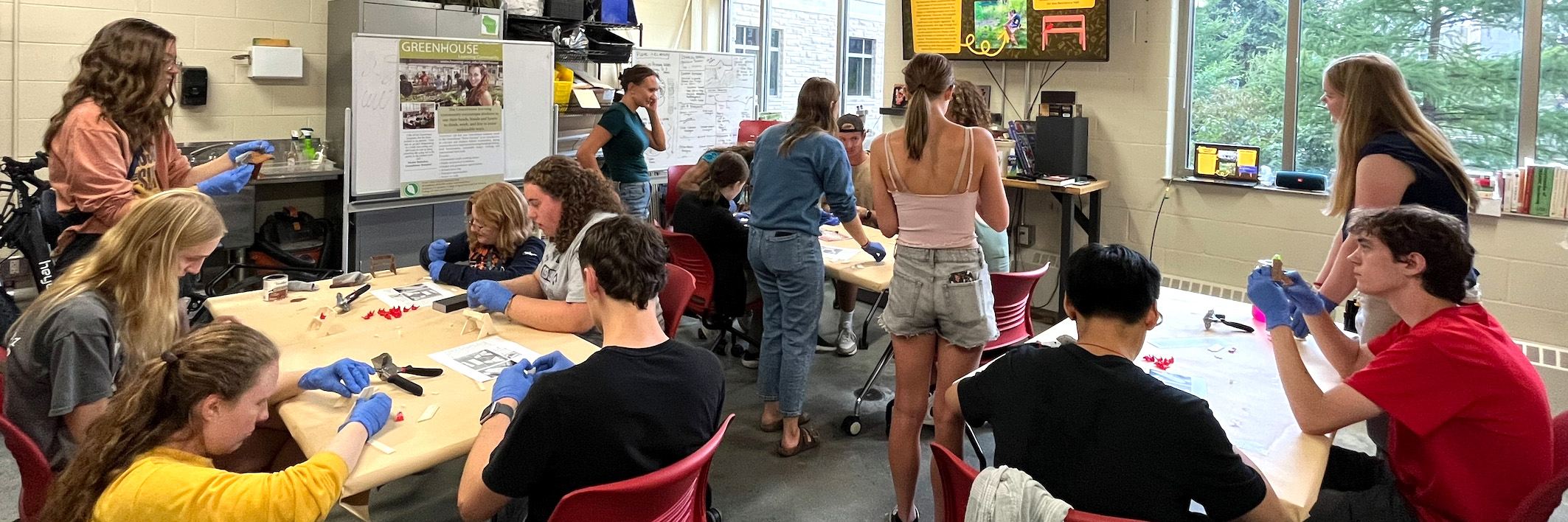 Groups of people sit at tables and benches creating crafts from wood