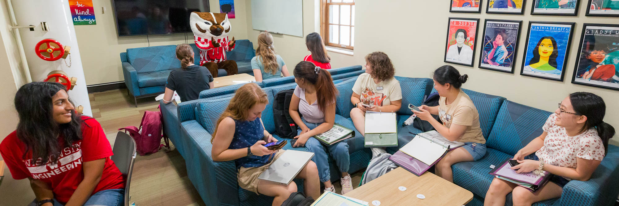 A group of people sit in a lounge studying while Bucky Badger makes an appearance