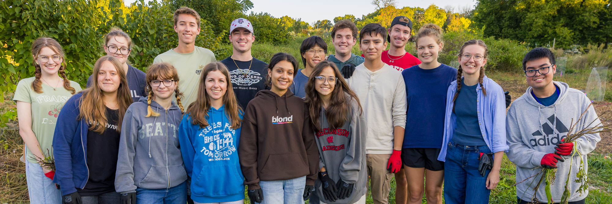 A group of people pose while holding weeds with a garden in the background.