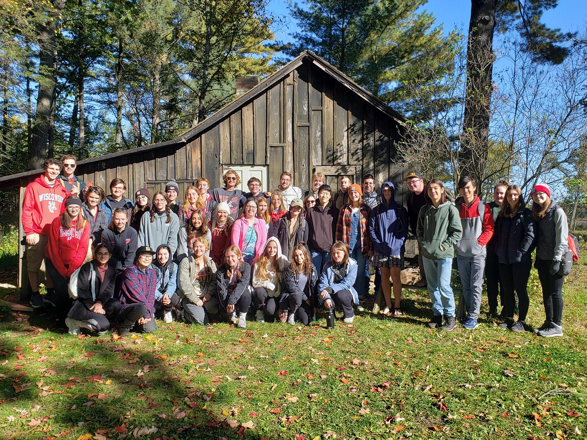 A group of people pose for a phone with Aldo Leopold's shack in the background