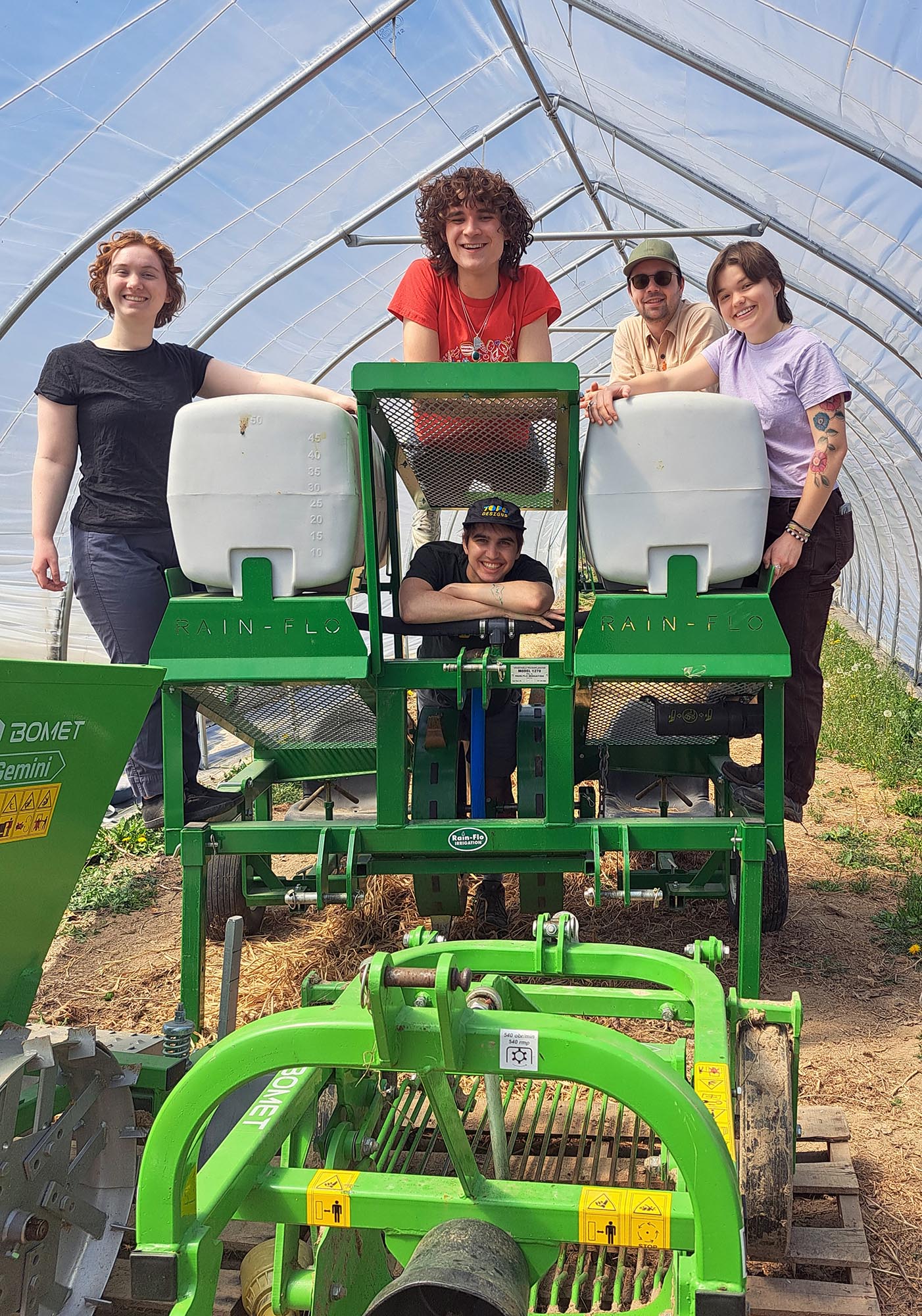 Five people pose for a photo while standing on a piece of farm machinery.