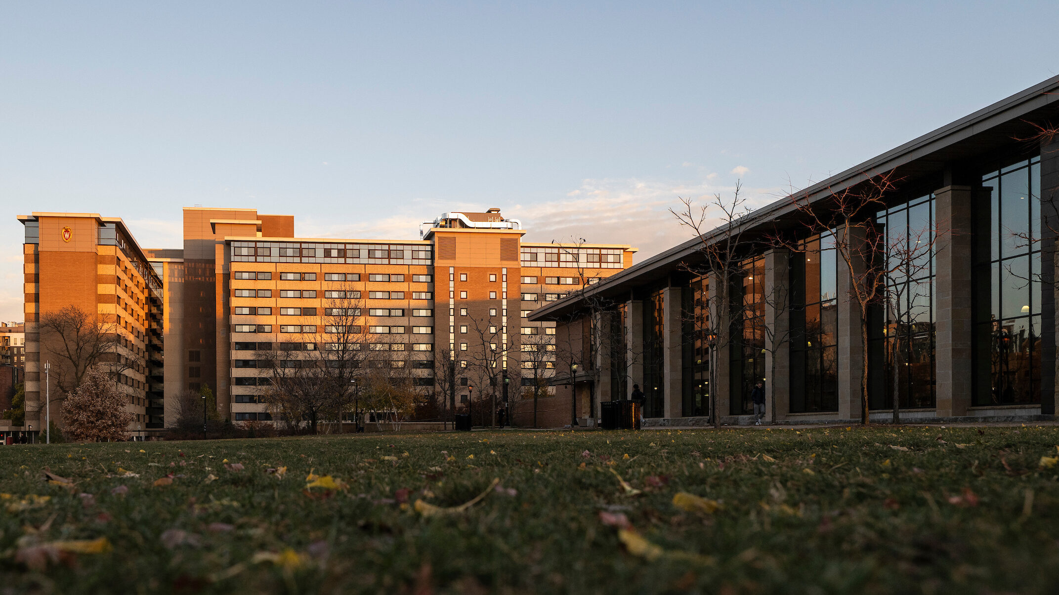 Witte Residence Hall and the Gordon Dining & Event Center at sunset with grass and leaves in the foreground.