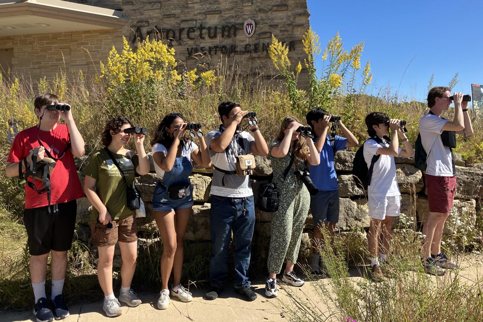 Eight people look through binoculars for dragonflies at the UW Arboretum Visitor Center.