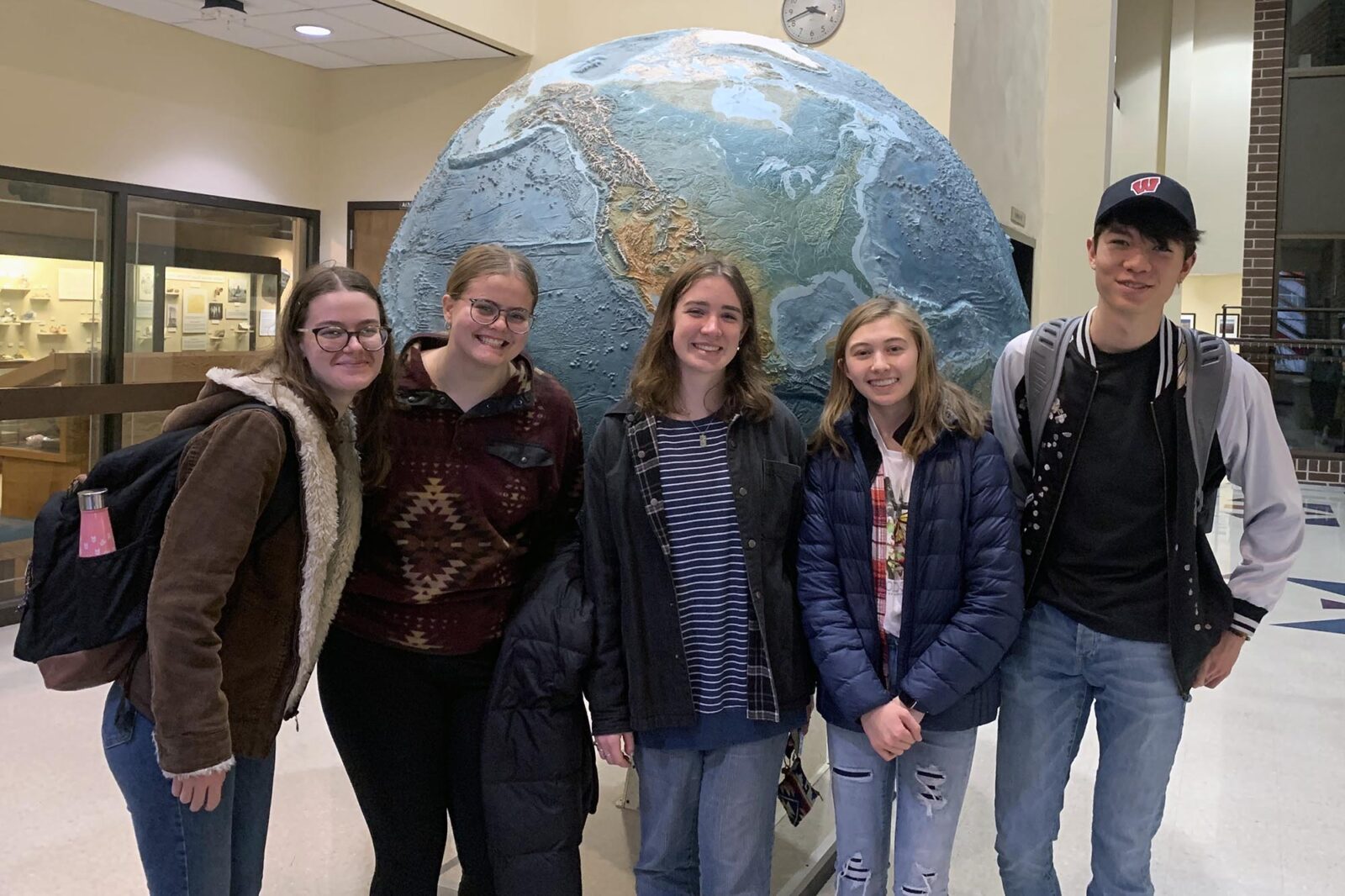 Five people pose in front of a globe of the Earth.