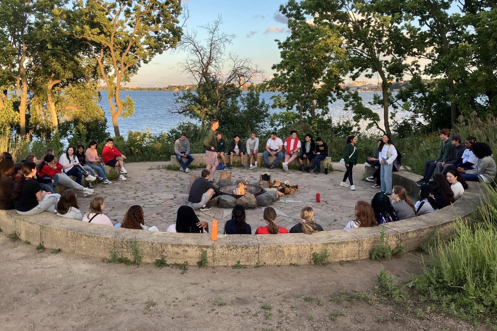 A group of people sitting in a fire circle around a fire at Picnic Point.