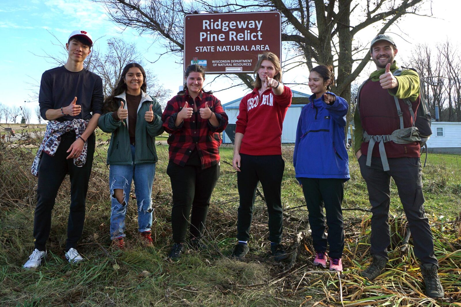 Six people pose for a photo at Ridgeway Pine Relict State Natural Area while giving the thumbs up and pointing at the camera.