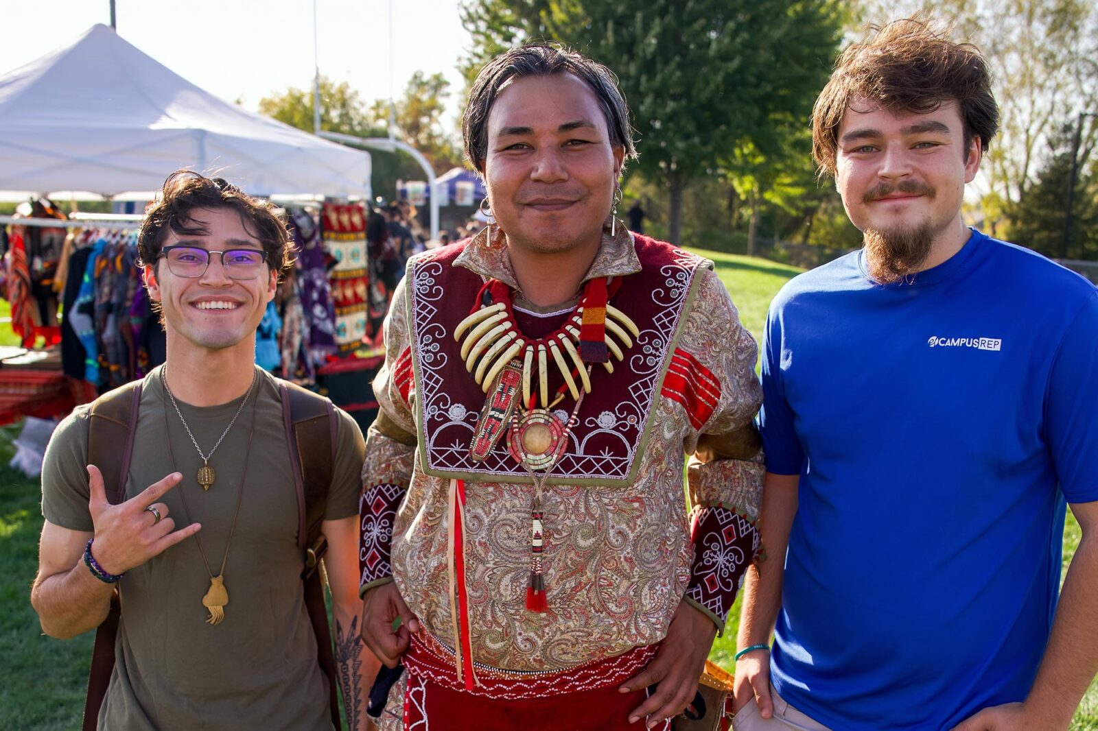 Three people pose for a photo with the one in the center in traditional Native American dress.
