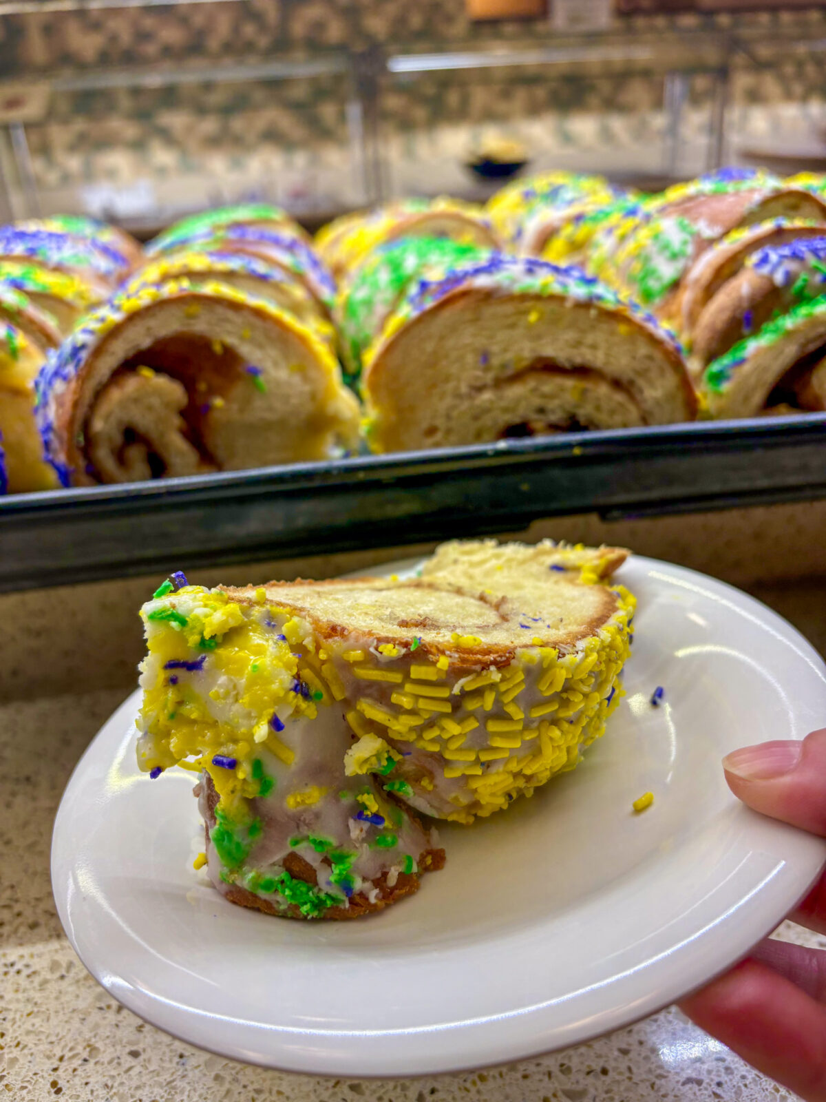Slice of King Cake on a plate with a tray full behind at dining's Mardi Gras event