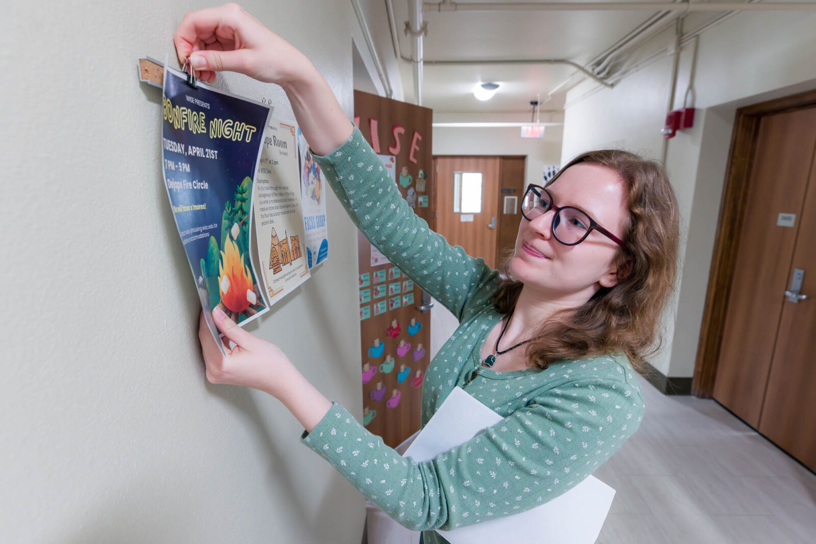 Elise puts up a flyer for a WISE Learning Community event in Waters Residence Hall.