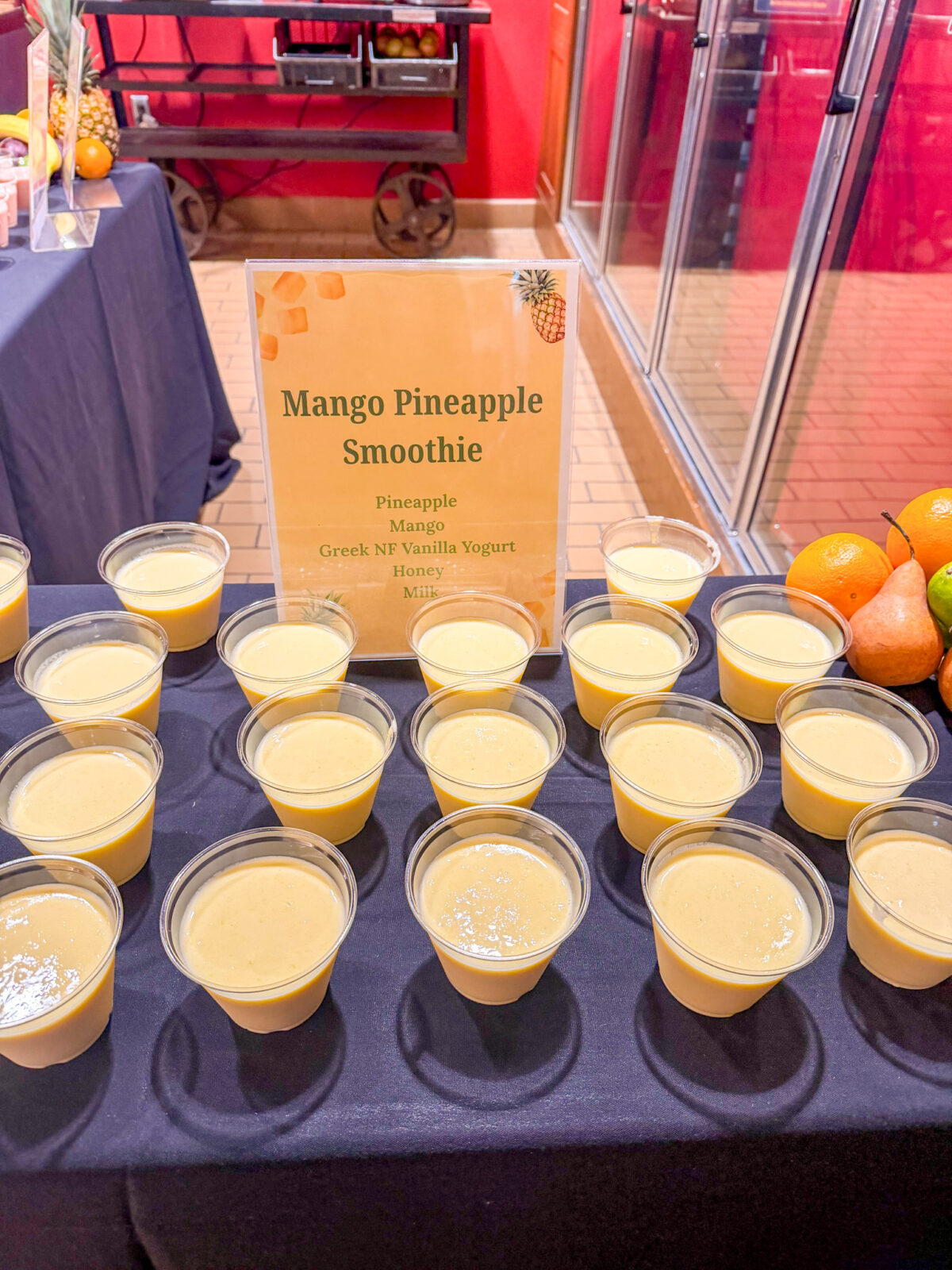 Mango Pineapple Smoothie sign and small cups lined up for Fruit Smoothie Day