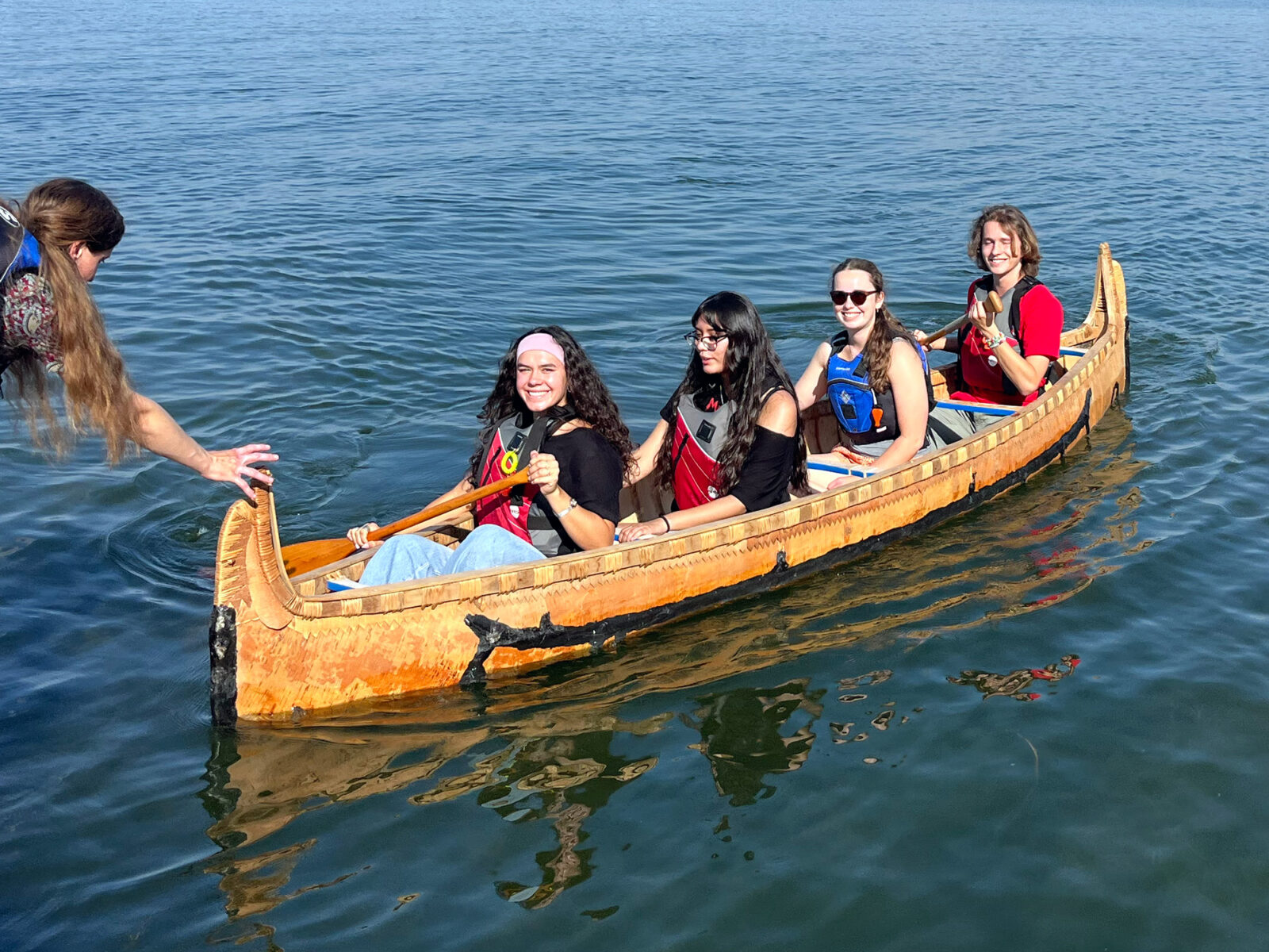 Four Spark residents paddle in a birch bark canoe on a lake.