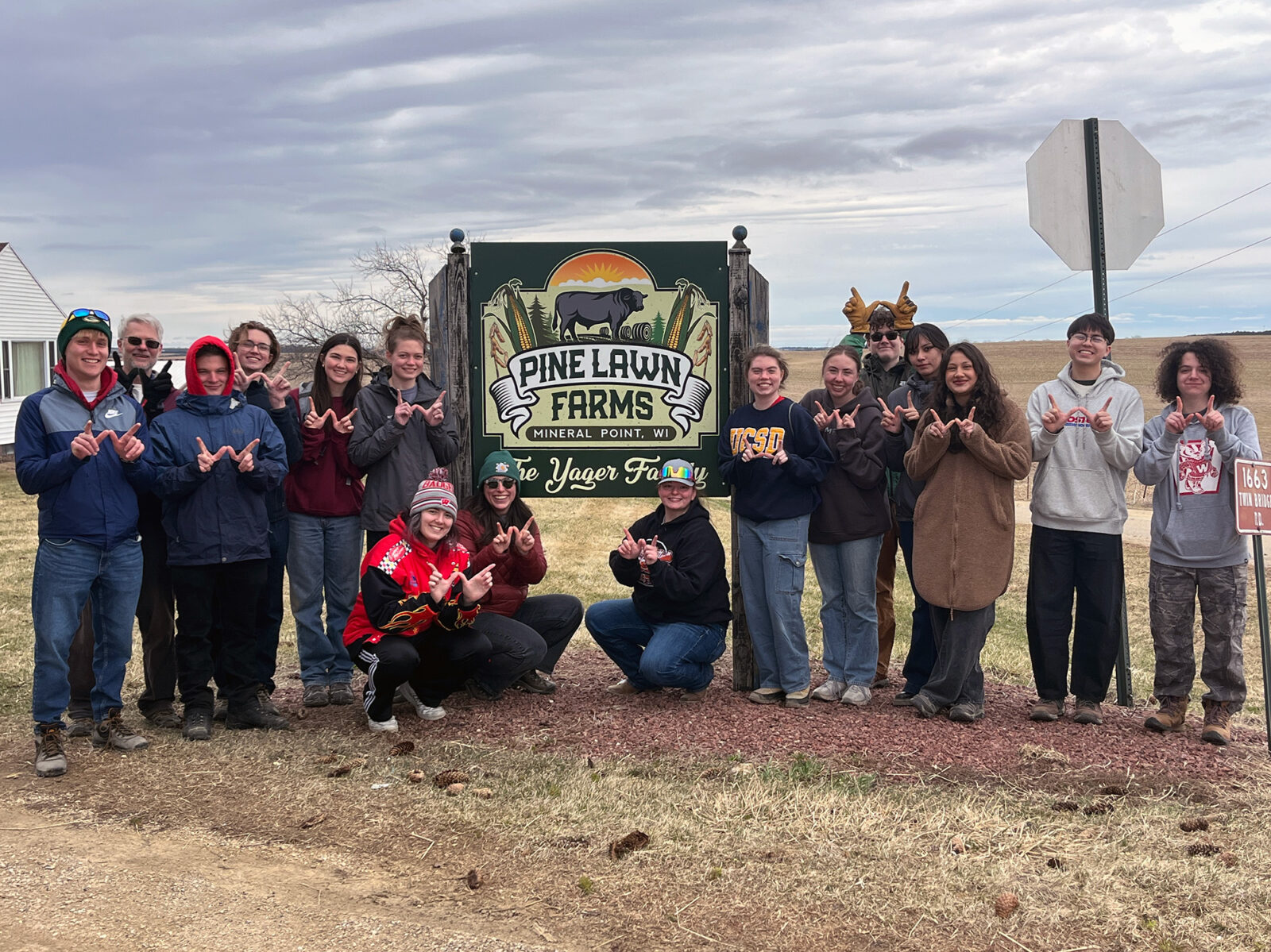 A group of Spark residents pose for a photo while making the letter "W" with their hands in front of a sign for Pine Lawn Farms.