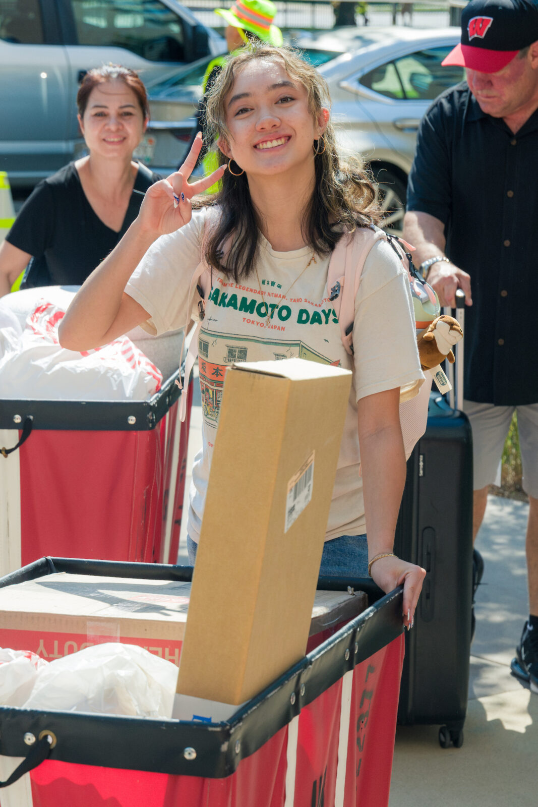 A person flashes the peace sign with their hand while pushing a red moving cart