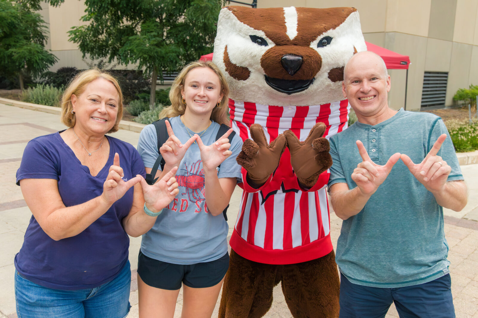 Bucky poses with parents and a student while making the letter "W" with their hands