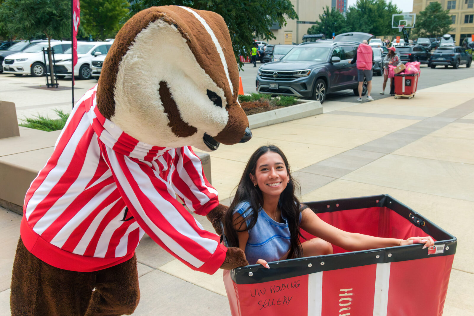 Bucky Badger pushes a person in a red moving cart